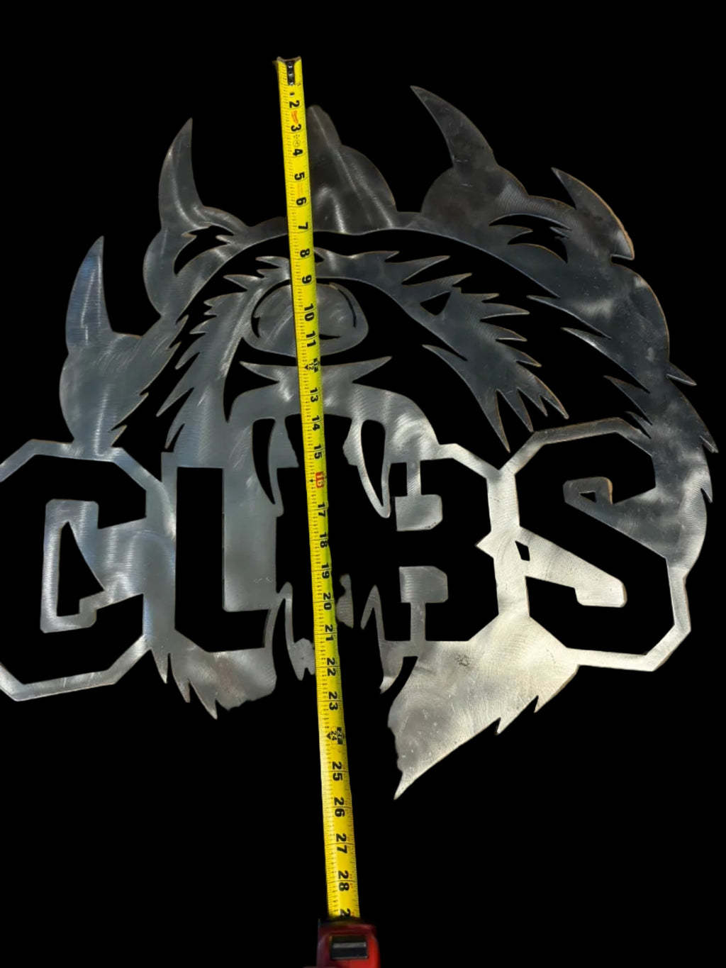 Metal wall art of a Bear biting the word Cubs with a measuring tape for scale on a cardboard background